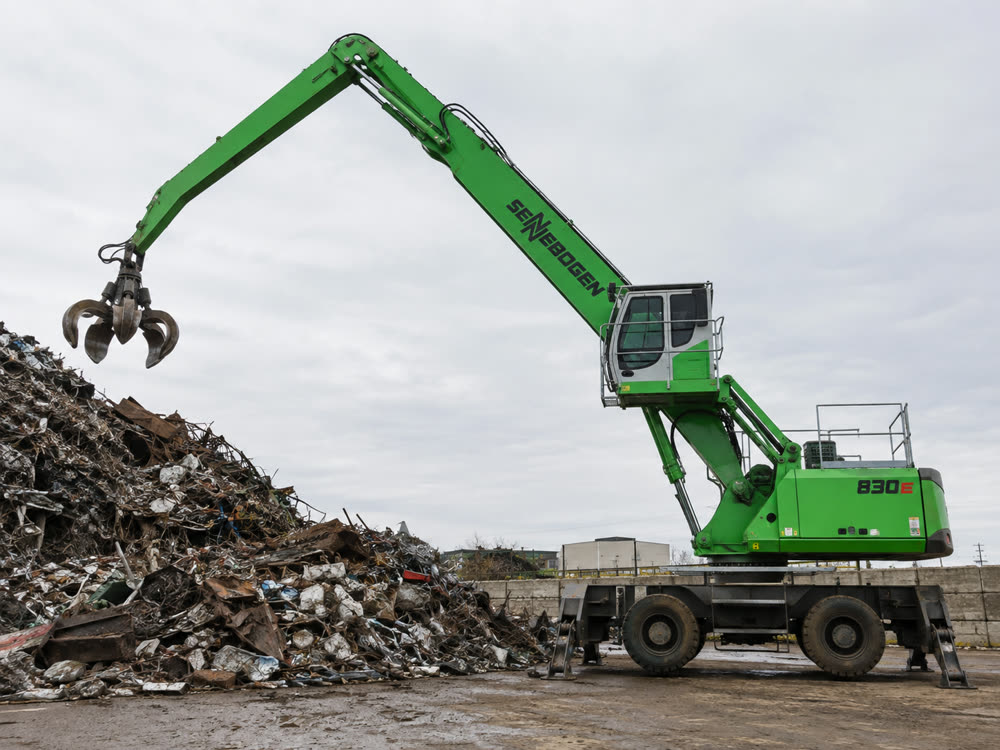 A material handler holds its open grapple above a scrap pile.